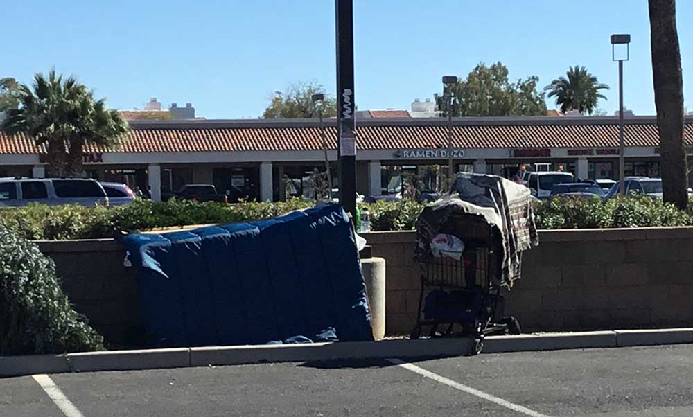 homeless man sleeping in makeshift tent next to shopping cart